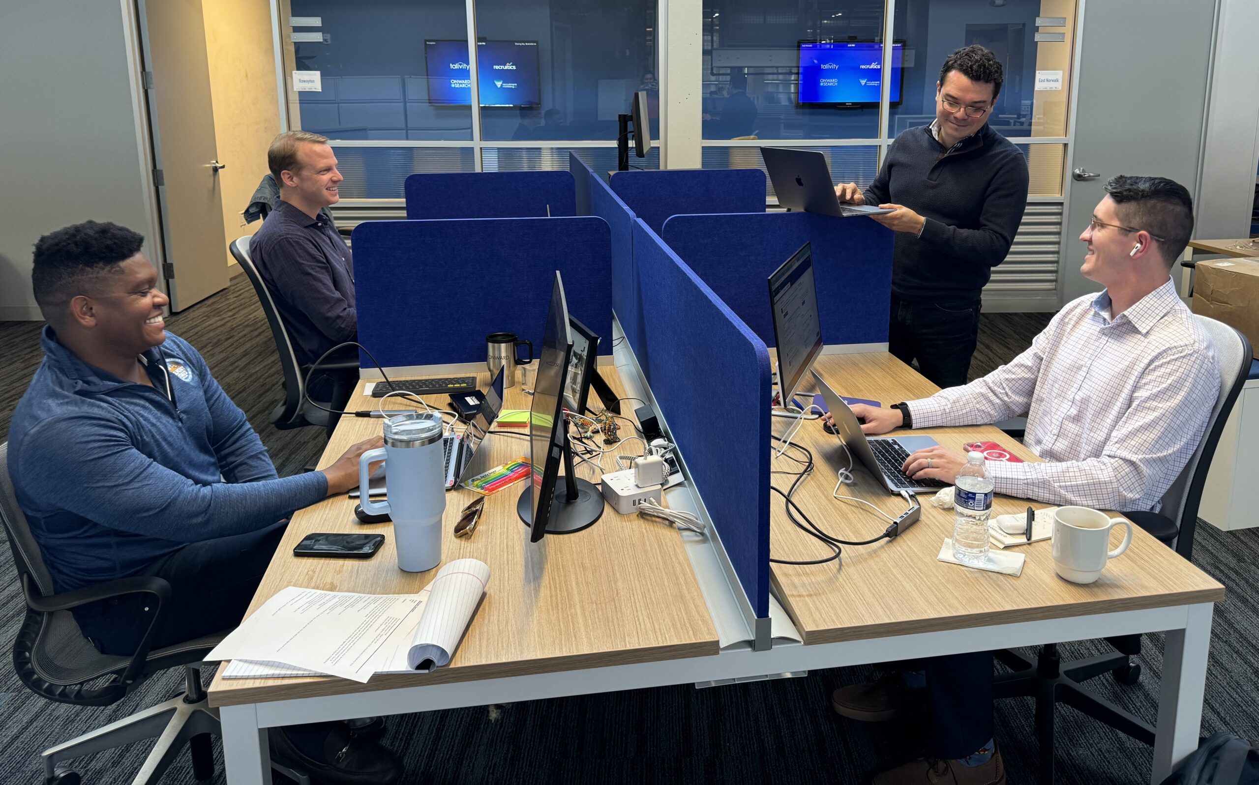 Picture of four male members of the Onward Accessibility team collaborating at their desks in our corporate headquarters.