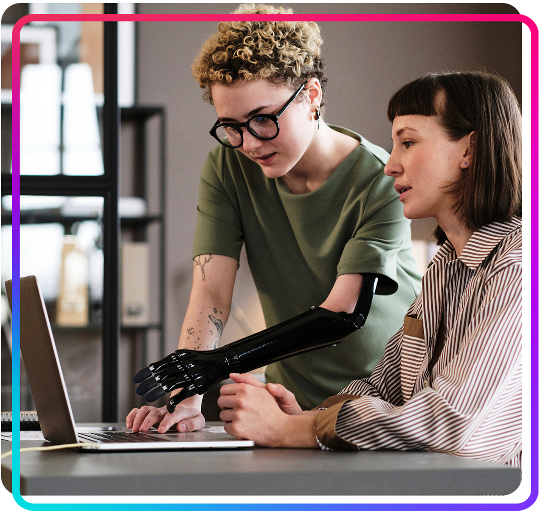 Young woman with prosthetic arm pointing at laptop and talking to her colleague while working on an digital accessibility audit at the office.